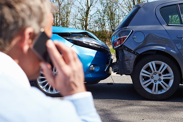 Man on a cell phone standing next to a car accident in Oakland, CA
