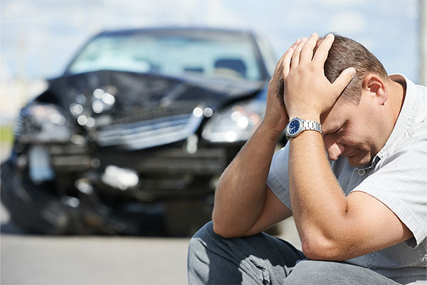 Man sitting outside of car on curb holding his head in his hands after a car accident in Oakland, CA