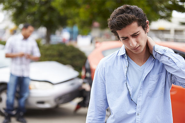 Young man holding the back of his neck and standing beside a car accident in Oakland CA