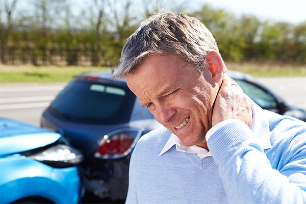 man standing next to a car accident holding the back of his neck with a whiplash injury in Oakland, CA